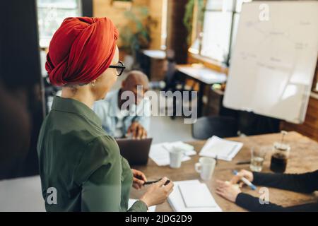 Chef d'équipe musulman ayant une réunion avec ses collègues d'affaires dans une salle de réunion moderne. Bonne femme d'affaires ethnique portant un foulard dans un multiticultu Banque D'Images