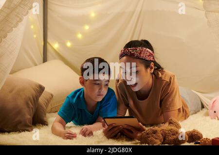 Mère lisant un livre électronique à son fils lorsqu'ils sont couchés sur le sol dans une grande tente Banque D'Images