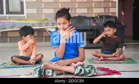 Groupe d'enfants engagés dans le yoga à la maison assis sur le tapis. Banque D'Images