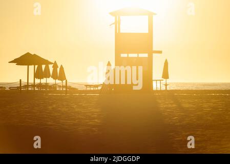 Silhouettes de tour de guet, chaises longues et parasols sur la plage de Piscinas dans le rétro-éclairage doré du soleil, Costa Verde, Sardaigne, Italie Banque D'Images