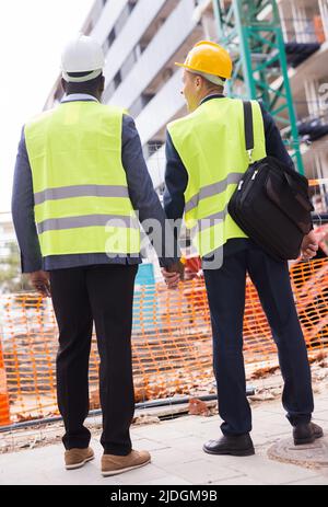 Deux architectes en casques de protection et veste regardent la maison inachevée. Vue de l'arrière Banque D'Images