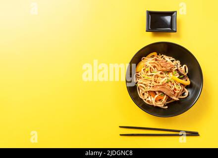 Cuisine asiatique. Cuisine chinoise classique ou japonaise, cuisine thaïlandaise de rue. Nouilles Udon en plaque noire sur fond jaune avec espace vide pour le texte. Top vie Banque D'Images