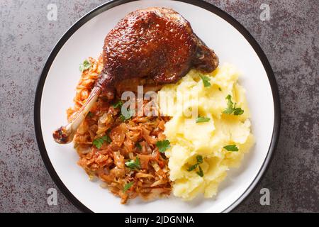 Aliments cuits cuisse de canard rôtie, ragoût de chou, pommes de terre bouillies en gros plan dans une assiette sur la table. Vue horizontale du dessus Banque D'Images