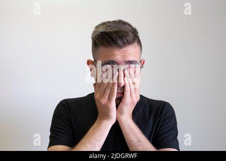 Jeune homme frottant les yeux, portrait de jeune homme fatigué frottant les yeux isolé sur fond gris. Adolescent de race blanche et brune. Banque D'Images