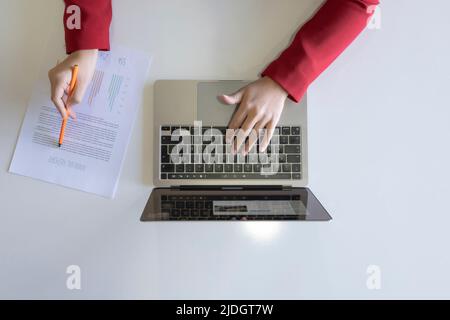 Travailler sur un ordinateur portable, vue de dessus d'une femme d'affaires travaillant sur un ordinateur portable et vérifier le rapport annuel avec un stylo. Contrôler, travailler sur des cartes concept photo. Banque D'Images