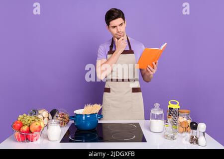 Photo de l'incertain ponder mari porter des tabliers gris lecture lourde long nouveau souper recette isolé couleur violet fond Banque D'Images