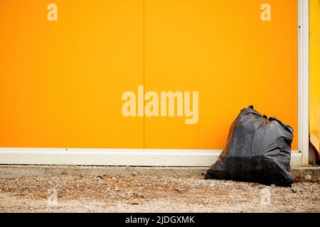 Sac poubelle en plastique noir dans la rue contre le mur jaune Banque D'Images