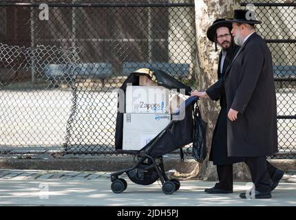 2 hommes juifs hassidiques, peut-être de la famille, marchent sur l'avenue Lee en utilisant une poussette pour porter des boîtes de chaussures Zappos. À Williamsburg, Brooklyn, New York. Banque D'Images