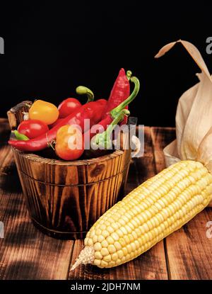 Épis de maïs avec piments et tomates légumes frais nourriture naturelle dans seau en bois, bio Banque D'Images