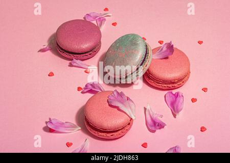 Macarons aux pétales de fleurs de pivoines sur fond rose. Dessert sucré, couleurs de bonbons colorées et pastel, concept d'été. Style romantique, carte de fête, Banque D'Images