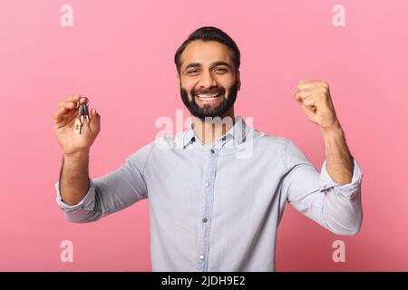 Un Indien excité tenant les clés et applaudisse, se levant le poing, un gars barbu se réjouissant isolé sur fond rose, a déménagé dans un nouvel appartement Banque D'Images