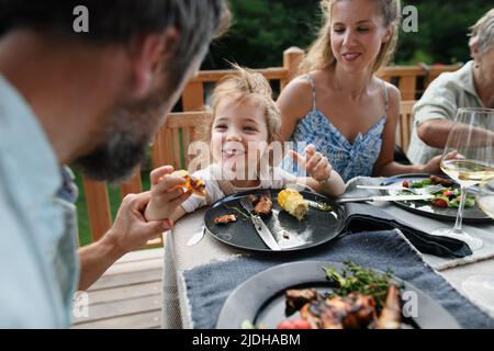 Repas de famille au barbecue dîner sur le patio, petite fille avec des parents assis à table et appréciant la nourriture. Banque D'Images