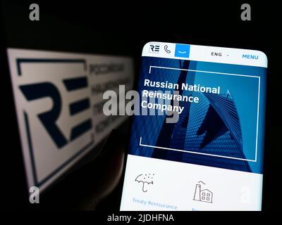 Personne tenant un téléphone portable avec la page Web de la Compagnie nationale russe de réassurance (RNRC) à l'écran devant le logo. Concentrez-vous sur le centre de l'écran du téléphone. Banque D'Images