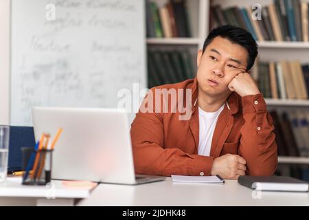 Malheureux enseignant asiatique assis au travail ayant des problèmes en classe Banque D'Images