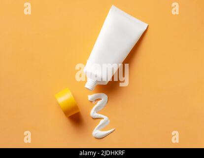 Tube cosmétique blanc avec crème solaire et texture crème pressée sur fond orange. Banque D'Images