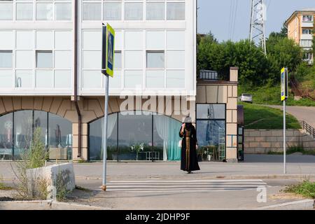 Une femme musulmane vêtue de noir national descend dans la rue de la ville, couvrant son visage des passants. Banque D'Images