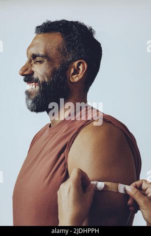 profil adulte moyen souriant barbu vacciné avec les mains plaçant le plâtre sur le bras homme dans le studio coup de feu yeux fermé studio Banque D'Images