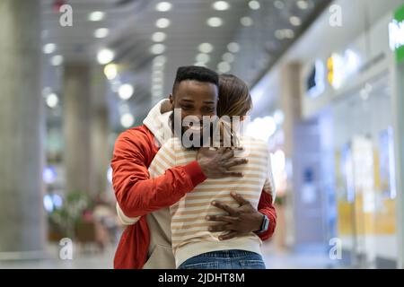 Un homme noir heureux rencontre une petite amie à l'aéroport après un long moment, couple se hembrassant à la porte d'arrivée Banque D'Images