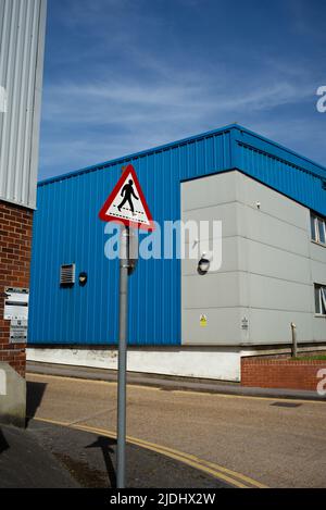Un panneau d'avertissement de sécurité rouge pour piétons qui traverse un fond bleu fort d'une unité industrielle moderne. Banque D'Images