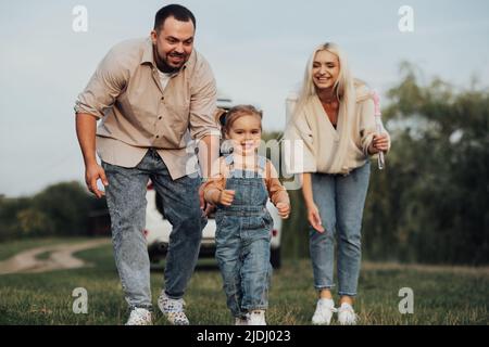 Bonne jeune famille s'amuser en plein air, petite fille jouant à la course loin de ses parents Banque D'Images