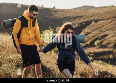 Femme gaie avec son Boyfriend tenant par les mains tout en randonnée sur la colline pendant le coucher du soleil, jeune couple profiter de leur voyage Banque D'Images