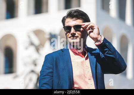 Homme d'affaires avec lunettes de soleil. Veste et chemise bleu. En arrière-plan un bâtiment. Banque D'Images