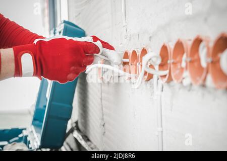 Gros plan sur le processus d'installation de la ligne des prises électriques murales réalisé par un électricien professionnel dans un immeuble de bureaux fraîchement construit. Construction Banque D'Images