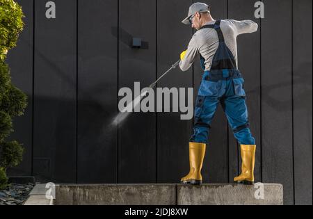 Travailleur caucasien dans son bâtiment moderne de 40s nettoyage mur sombre à l'aide d'un puissant nettoyeur à pression Banque D'Images