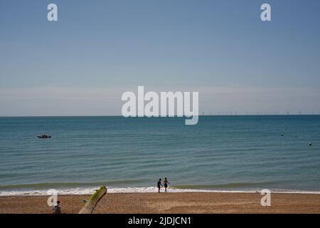 Brighton et Hove. Promenade en bord de mer entre Brighton et Hove. Une mer calme avec plage, canot de sauvetage et parc d'éoliennes de Rampion à distance. Banque D'Images