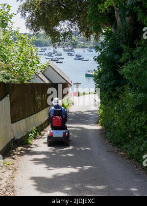 Senior en scooter de mobilité sur la route de la plage, Helford passage, Cornwall, Royaume-Uni Banque D'Images