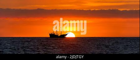 Une silhouette de navire se trouve à la mer tandis que le soleil s'élève sur l'horizon océanique Banque D'Images