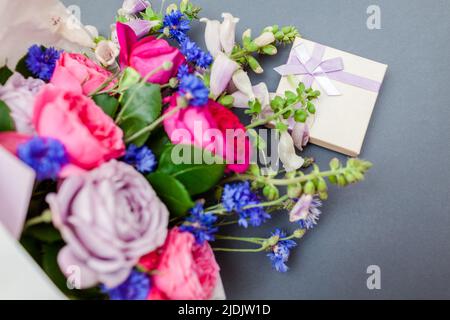 Gros plan du bouquet d'été de roses foxgants boutons de baccalauréat fleurs enveloppées dans du papier et disposées sur fond avec boîte-cadeau. Fleurs fraîches pour les LSS Banque D'Images