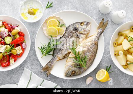 Dorada poisson mer bream cuit, salade grecque de légumes frais, pommes de terre bouillies à l'ail et aux olives et sauce tzatziki. Une alimentation saine. Régime méditerranéen. Banque D'Images