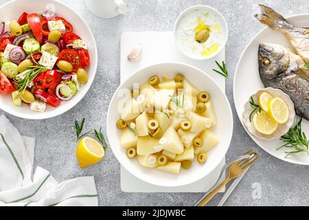 Pommes de terre bouillies à l'ail et aux olives, salade grecque de légumes frais, dorade de poisson cuite au four et sauce tzatziki. Une alimentation saine. Régime méditerranéen Banque D'Images