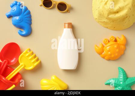 Bouteille de crème solaire pour bébé avec moules à sable, jouets, lunettes de soleil, chapeau sur table beige Banque D'Images