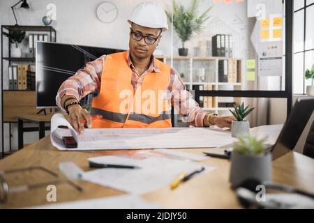 Portrait d'un architecte, d'un ingénieur ou d'un designer afro-américain assis à table et analysant des plans d'affichage assis à un bureau. Création du projet de construction. Banque D'Images