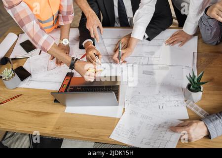 Gros plan d'architectes, d'ingénieurs et de concepteurs assis à table et analysant des plans. Des personnes de différents âges et de différentes races travaillant au bureau. Création du projet de construction. Banque D'Images