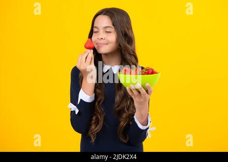 Un enfant de l'adolescence tient un bol à fraises sur fond jaune. Banque D'Images