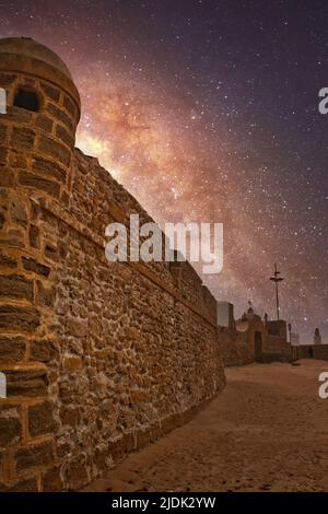 Paysage nocturne avec la voie lactée sur les vieux murs de pierre de la plage de la Caleta à Cadix, Espagne Banque D'Images