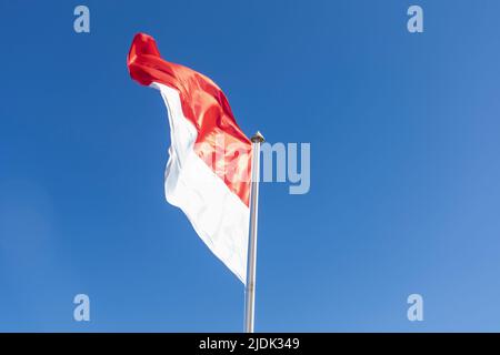 Drapeau national de la Principauté de Monaco agitant contre le ciel bleu. Vue basse. Copier l'espace. Banque D'Images