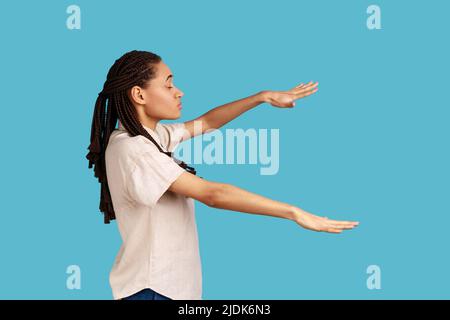 Vue latérale d'une femme aveugle avec des mains tendues marchant seul avec des yeux fermés dans l'obscurité, se sent désorientée, la route perdue, portant une chemise blanche. Studio d'intérieur isolé sur fond bleu. Banque D'Images