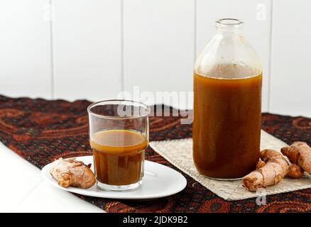 Boisson au curcuma et au Tamarind ou Kunyit Asam, boisson traditionnelle indonésienne à base d'herbes sur fond blanc et Batik Banque D'Images