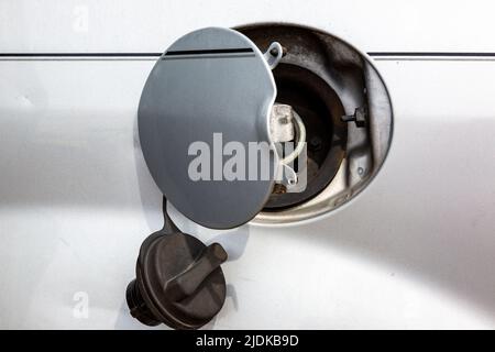 Un bouchon à essence est suspendu à une trappe de remplissage de carburant ouverte sur une voiture blanche. Banque D'Images