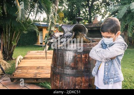 Garçon en colère dans une ferme à l'extérieur portant un masque médical et une veste en denim Banque D'Images