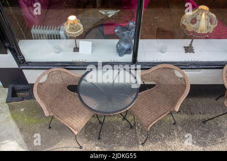 deux chaises et une table ronde à l'extérieur sur le trottoir à côté d'une fenêtre de magasin avec lampes de table Banque D'Images