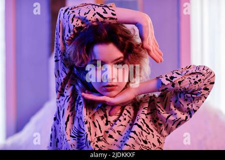 Portrait en gros plan de danseuse de mode féminine regardant l'appareil photo dans la lumière du néon avec la mise au point sur les mouvements de la main Banque D'Images