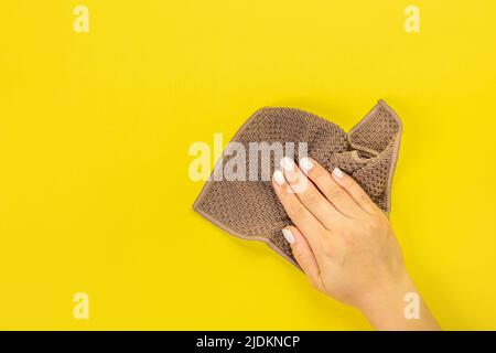 La main d'une femme au foyer tient un chiffon pour épousseter ou laver. Espace vide pour le texte ou le logo sur fond jaune. Début du printemps ou nettoyage régulier. Nettoyage Banque D'Images