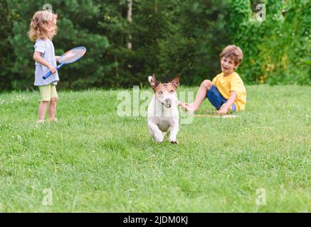 Chien mal espiègle volant un birdie de badminton d'enfants jouant avec des raquettes sur gazon vert Banque D'Images