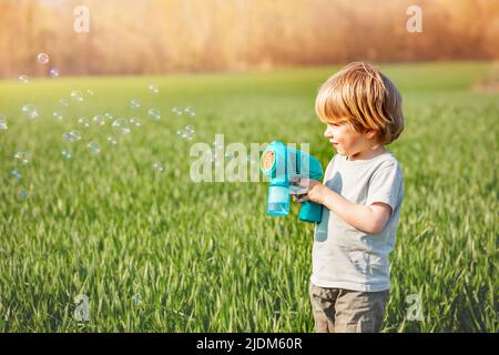 Garçon joue des bulles de savon debout ensemble sur le champ vert de printemps Banque D'Images