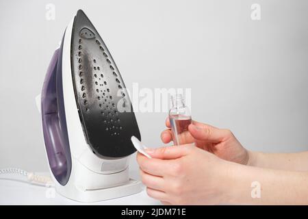Une femme nettoie la semelle du fer de la suie et de la tartre avec une solution spéciale dans une bouteille et un tampon de coton. Banque D'Images